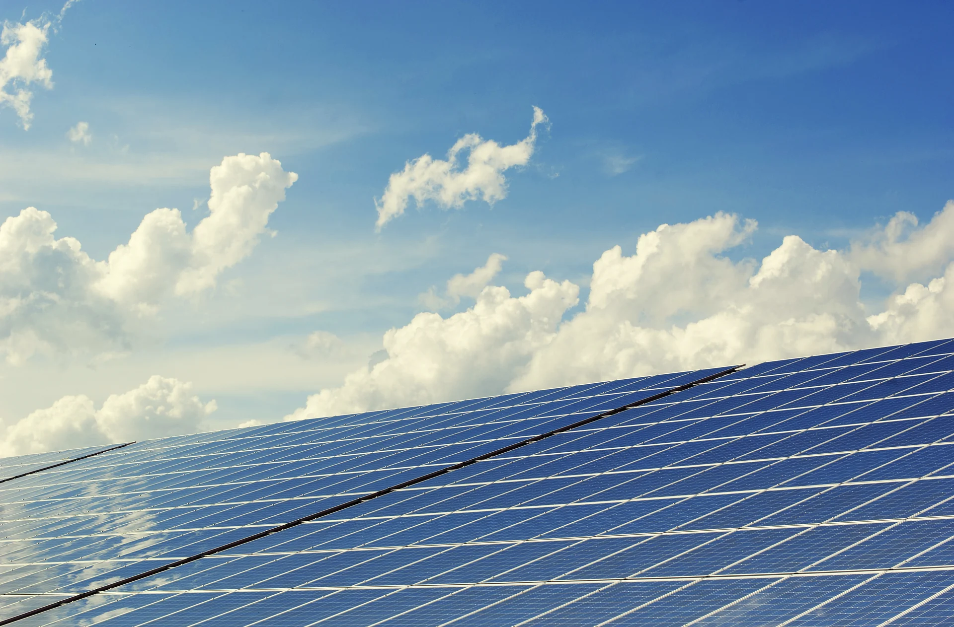 Solar panels angled toward a bright blue sky with white clouds